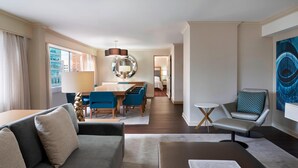 A modern hotel room with a grey sofa, a dining table with blue chairs, a small round table, and a large abstract painting on the wall. - Sheraton Ottawa Hotel (Ottawa)