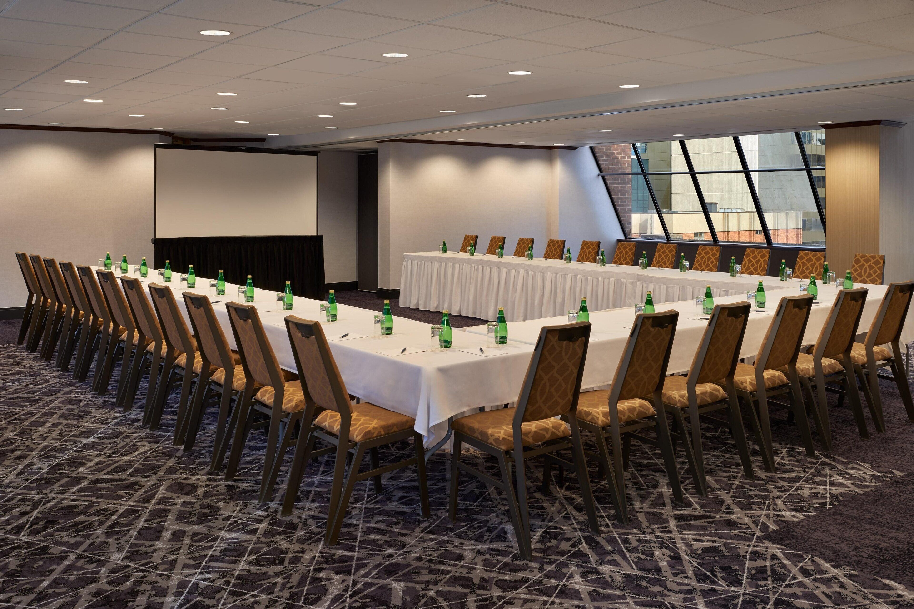 A conference room with a long table, chairs, and a projector screen.