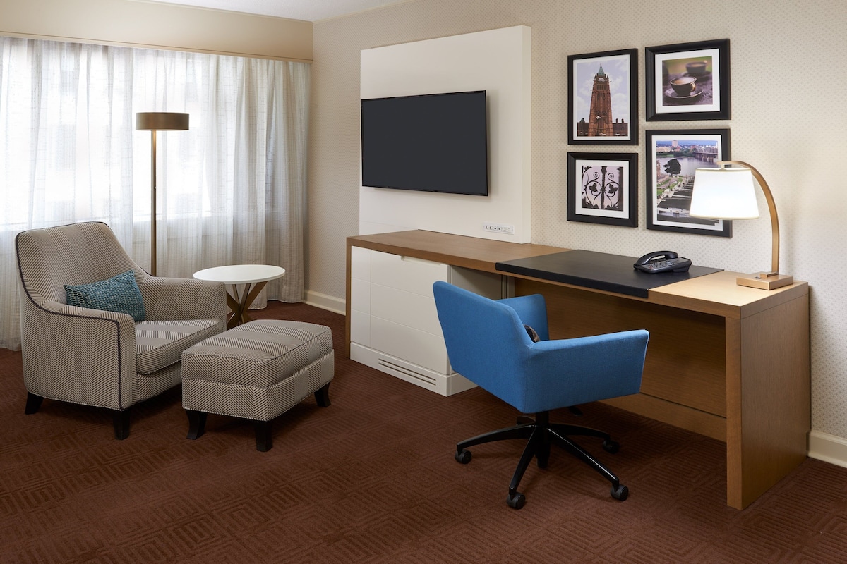 Habitación de hotel con escritorio, dos sillas, televisor y cuadros en la pared.