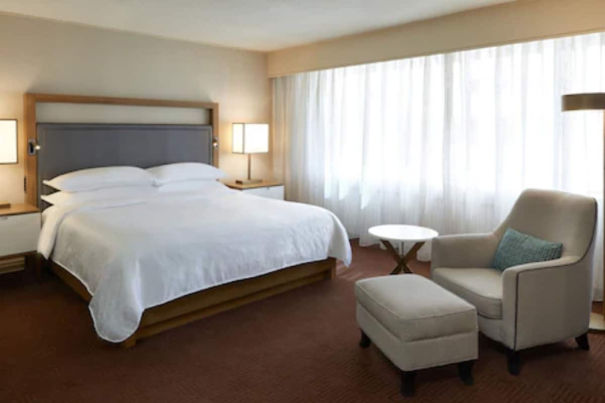 A hotel room with a large bed, a chair, a small table, and a lamp.
