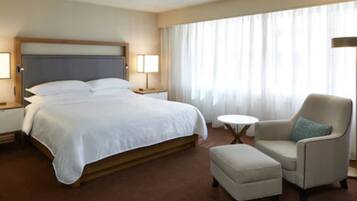 Una habitación de hotel con una cama grande, una silla, una mesita y una lámpara.