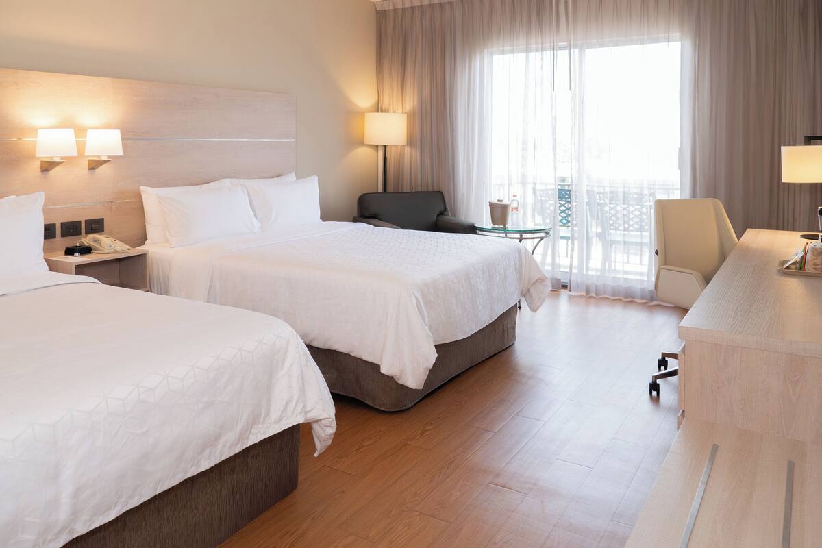 A hotel room with two beds, a desk, a chair, and a balcony with a table and chairs.