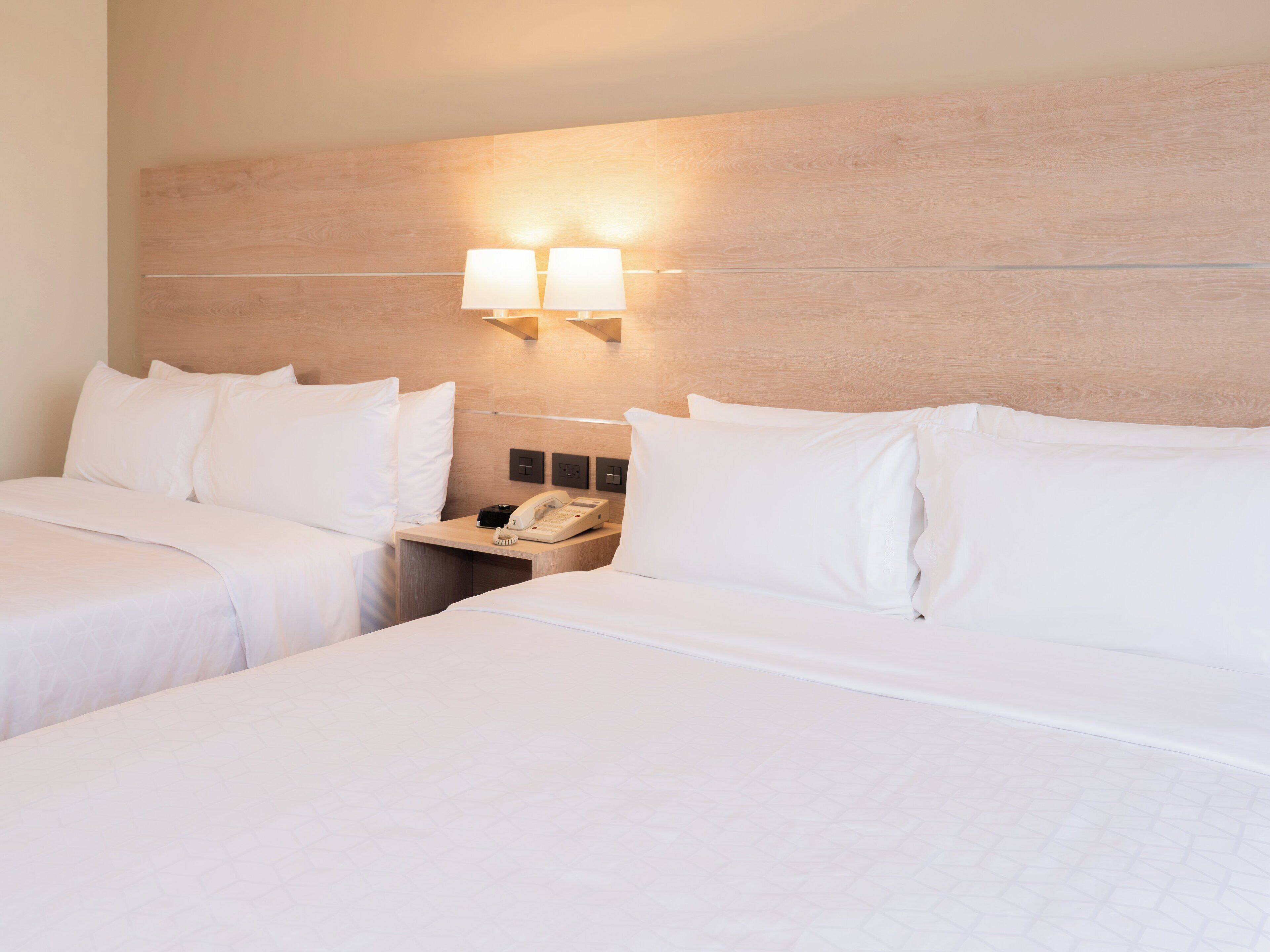 Ein Hotelzimmer mit zwei Betten, einem Nachttisch mit Telefon und Wandlampen.