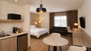 Habitación de hotel con cama, sofá, mesa de comedor, televisor y kitchenette.