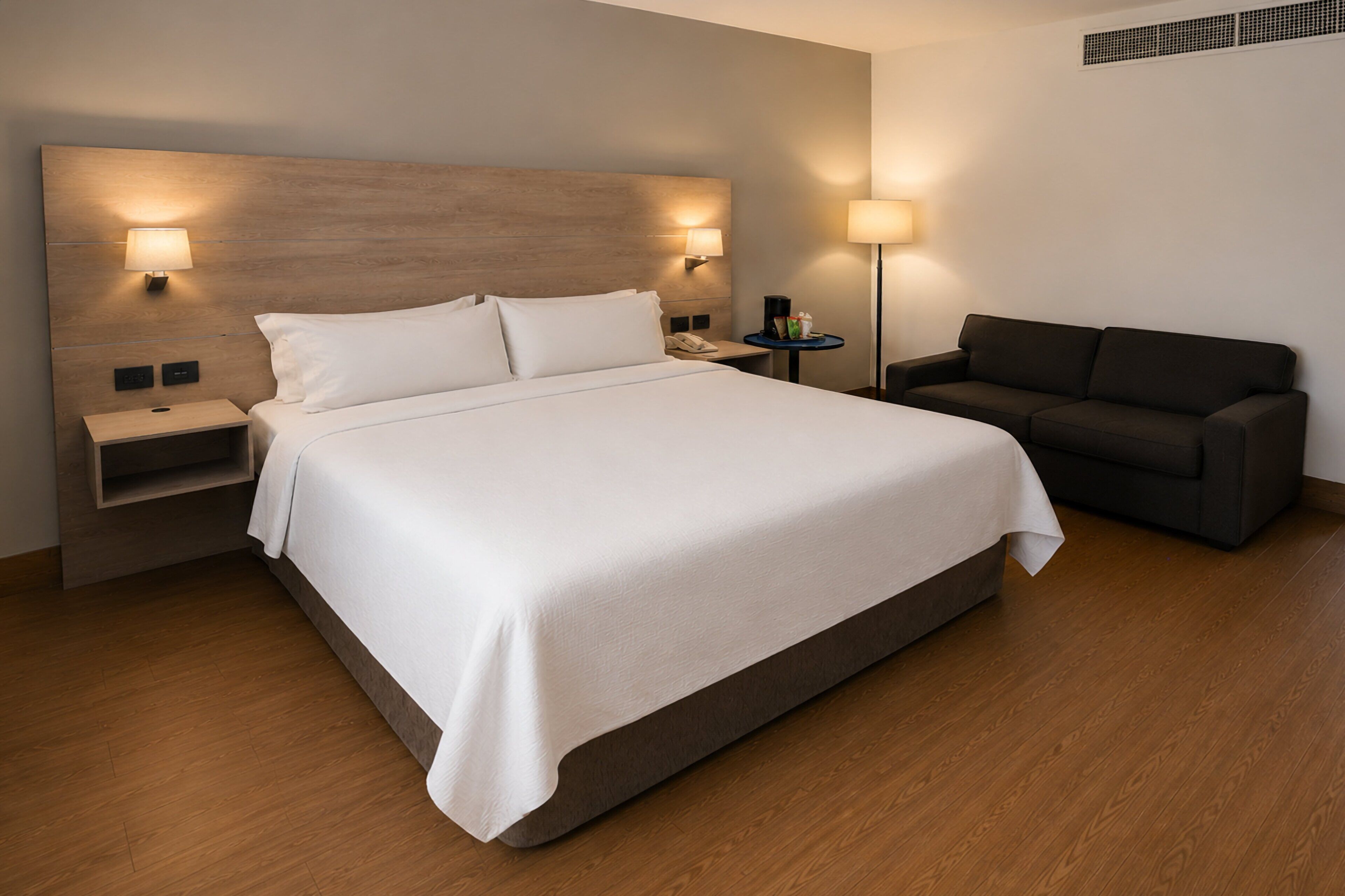 A hotel room with a large bed, bedside tables, a sofa, and wall-mounted lamps.