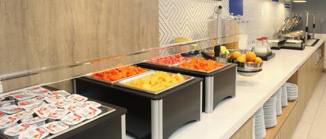 A buffet with labeled sections for fruits and cereals, including various fruits and yogurt containers.