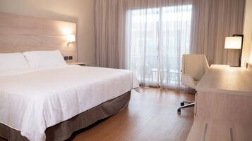 Habitación de hotel con una cama grande, un escritorio, una silla y una ventana con cortinas translúcidas.