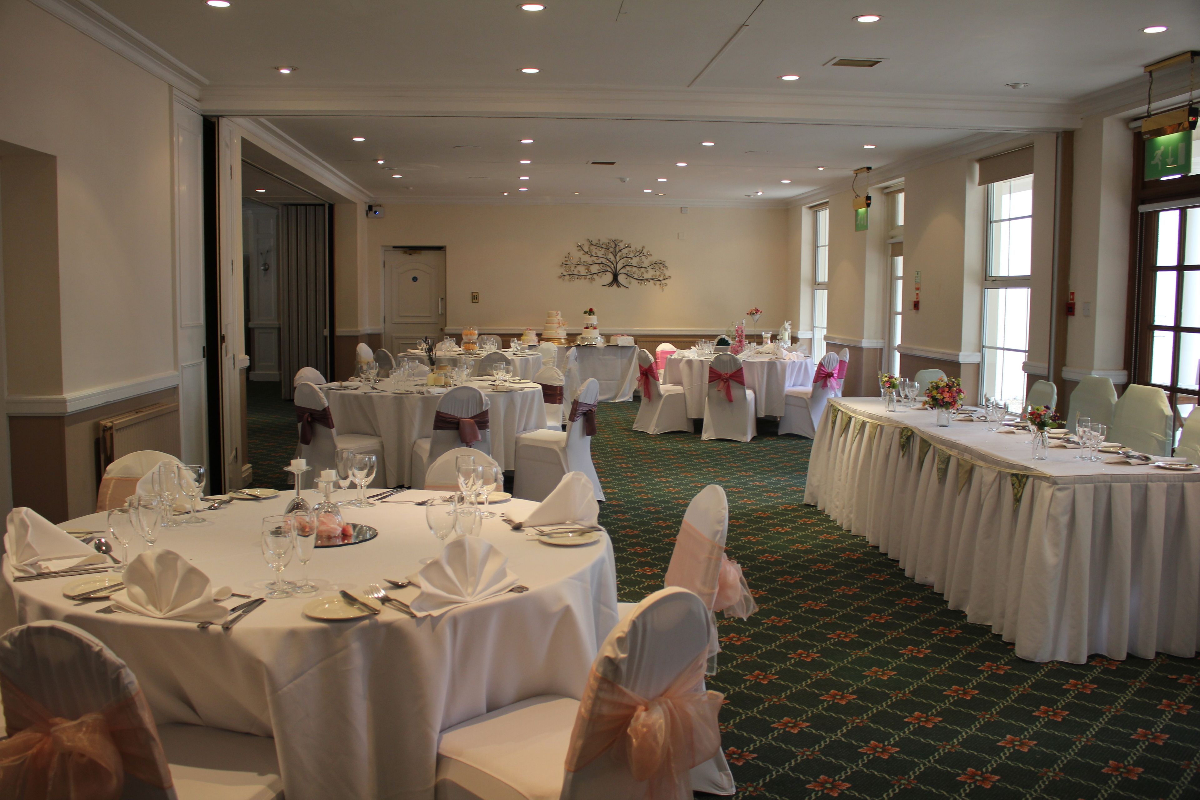 A banquet hall with round tables set for a formal event, featuring white tablecloths and chairs with bows.