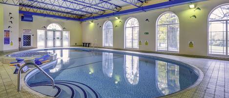 An indoor swimming pool with clear water, a tiled floor, and multiple windows.