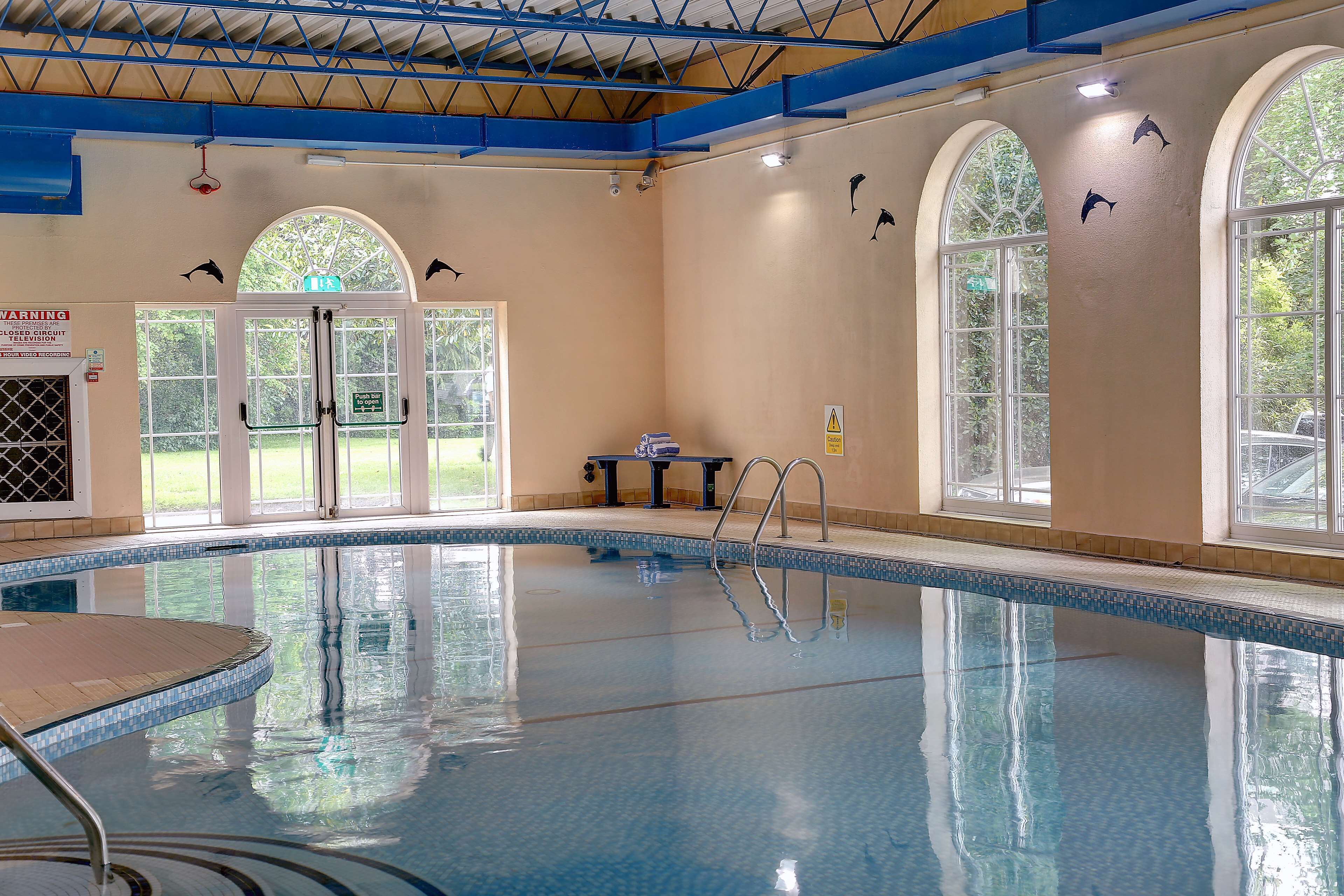 An indoor swimming pool with clear water, a diving board, and arched windows.