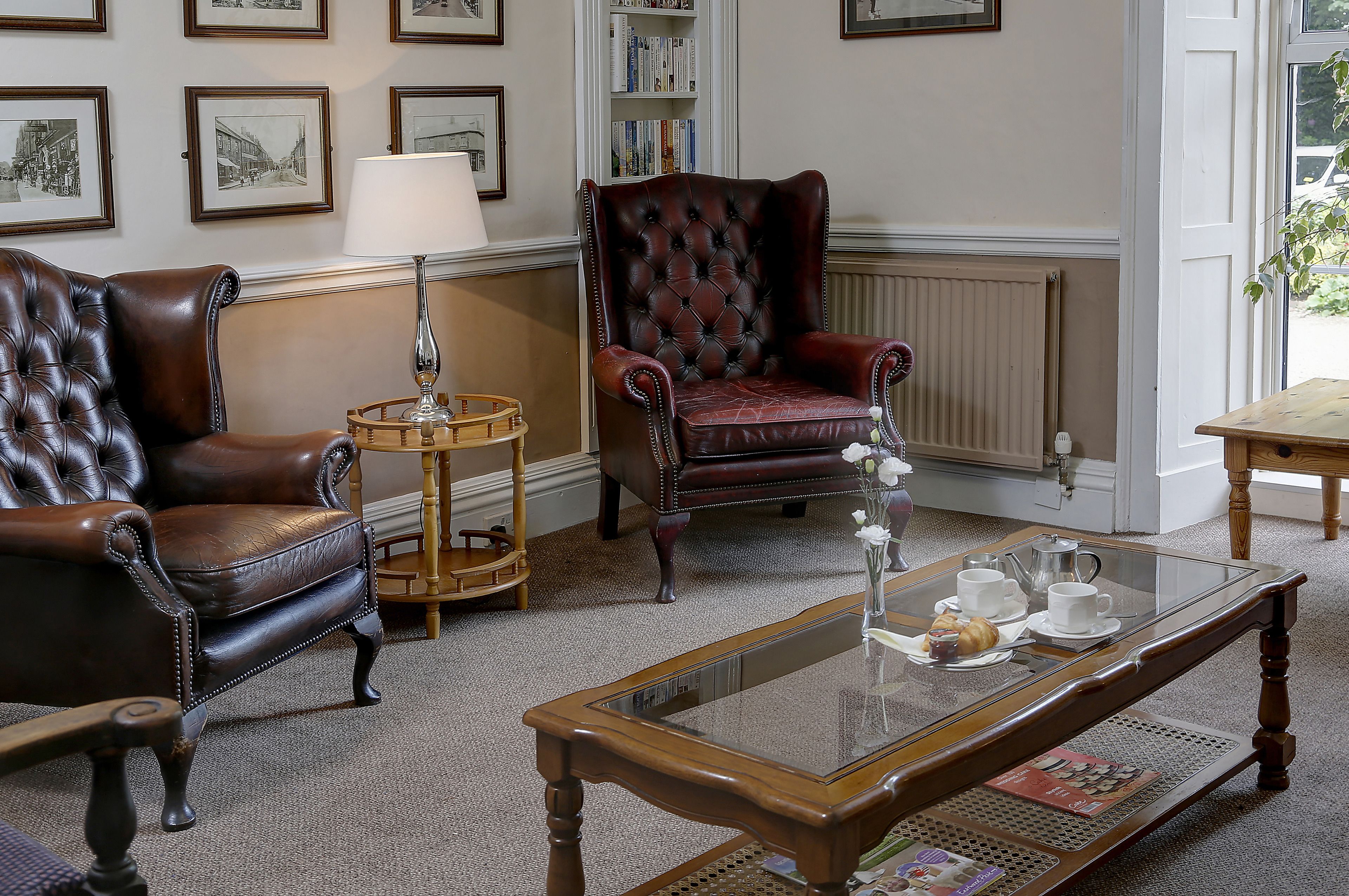 A room with two leather armchairs, a wooden coffee table with a glass top, and a bookshelf in the background.