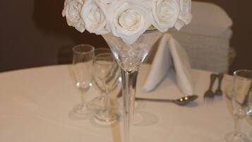 Une table avec un plateau en verre transparent, un grand vase en verre contenant des roses blanches et une serviette blanche pliée.