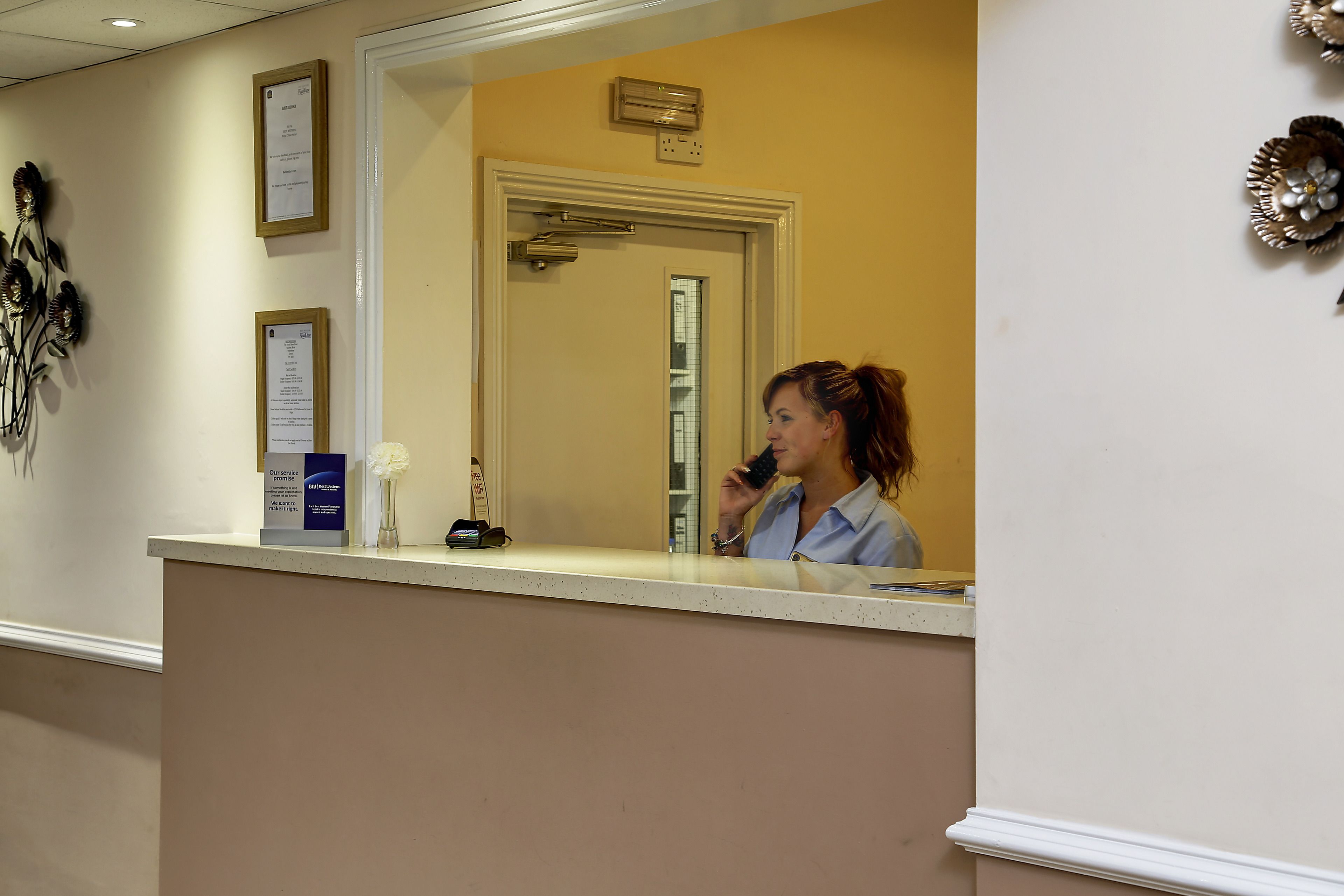 A reception desk with a mirror, framed certificates, and a small vase with flowers.