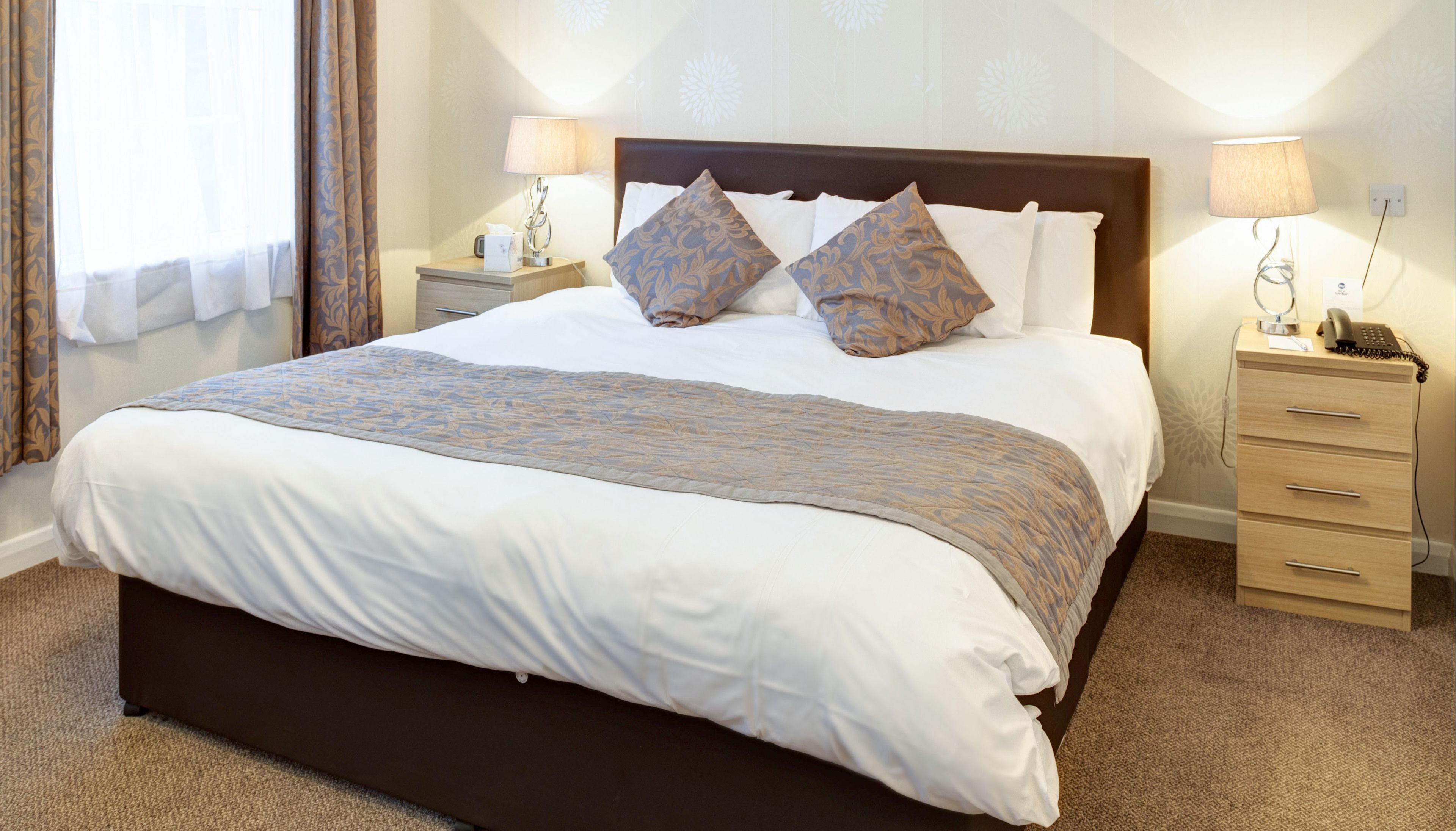 A neatly made bed with a patterned blanket, two bedside lamps, and a nightstand with a phone.