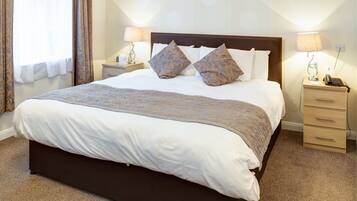 A neatly made bed with a patterned blanket, two bedside lamps, and a nightstand with a phone.