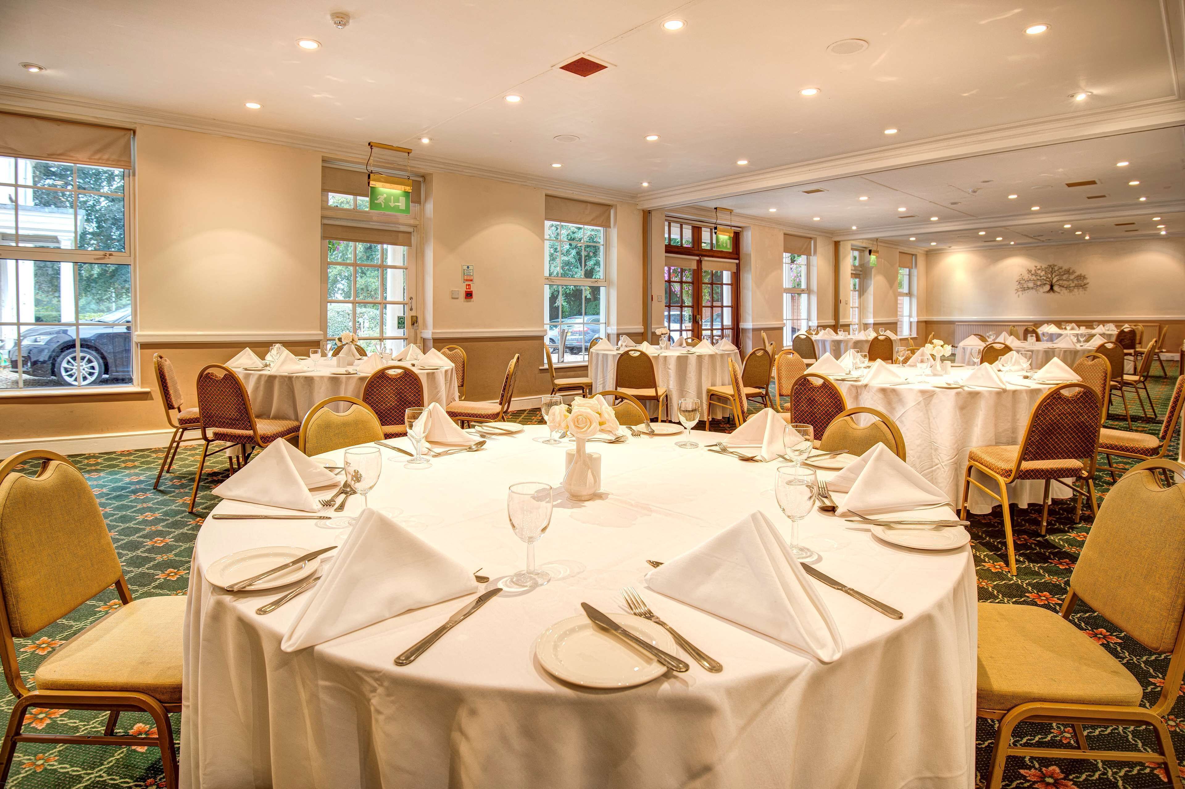 A banquet hall with round tables set for dining, each with white tablecloths, chairs, and basic tableware.