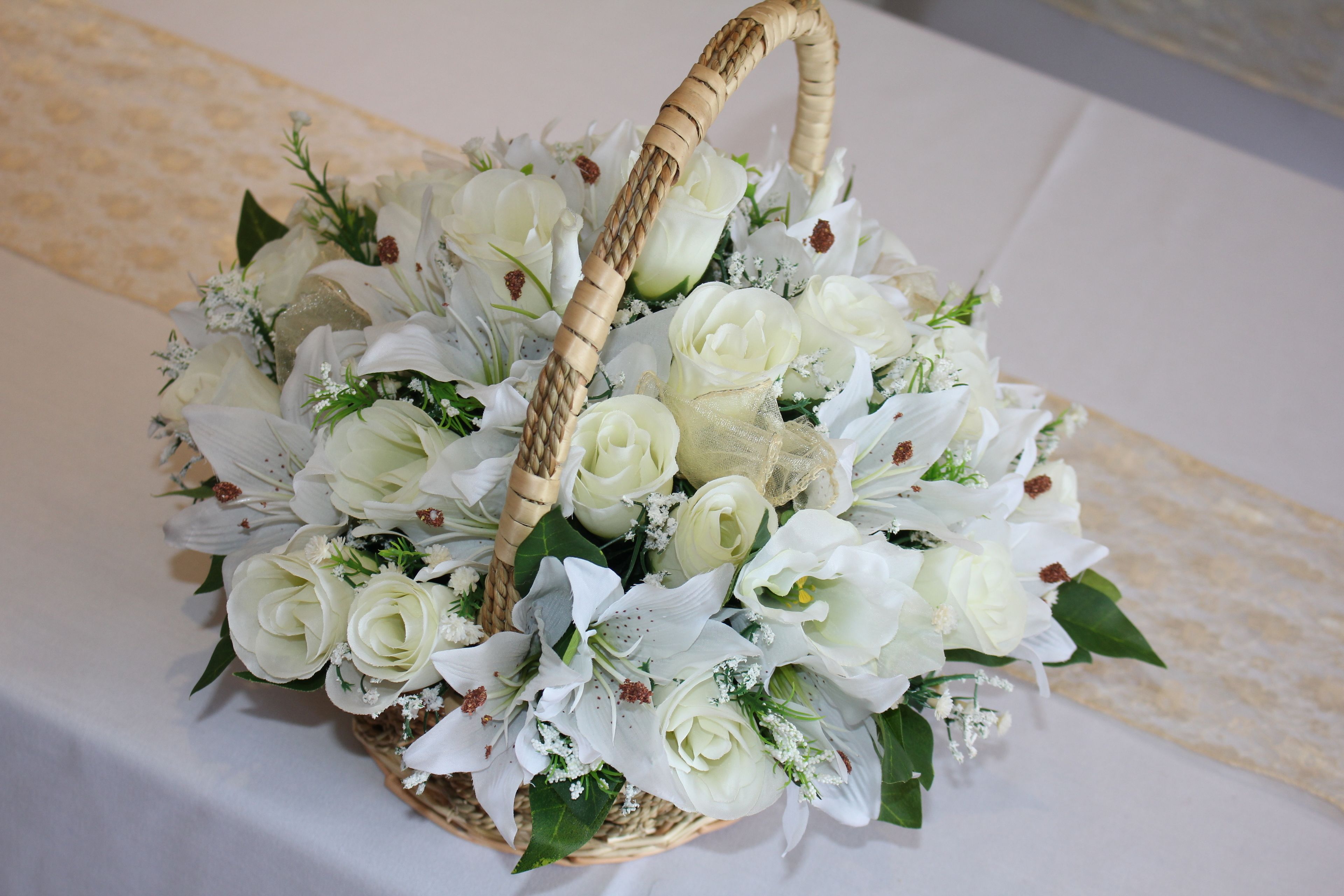 A wicker basket filled with white flowers and greenery, placed on a table with a patterned tablecloth.
