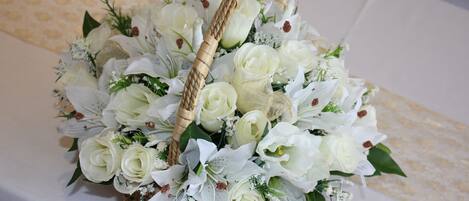 A wicker basket filled with white flowers and greenery, placed on a table with a patterned tablecloth.