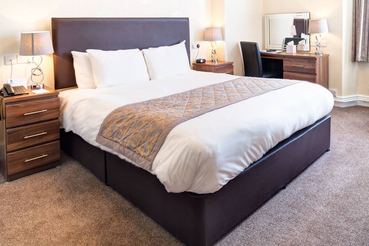 A neatly made bed with a patterned throw, a bedside table with a lamp, and a chair in a hotel room.