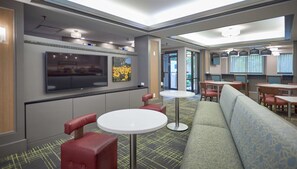 Een modern interieur met een bank, rode stoelen, een televisie en een eethoek met tafels en stoelen.