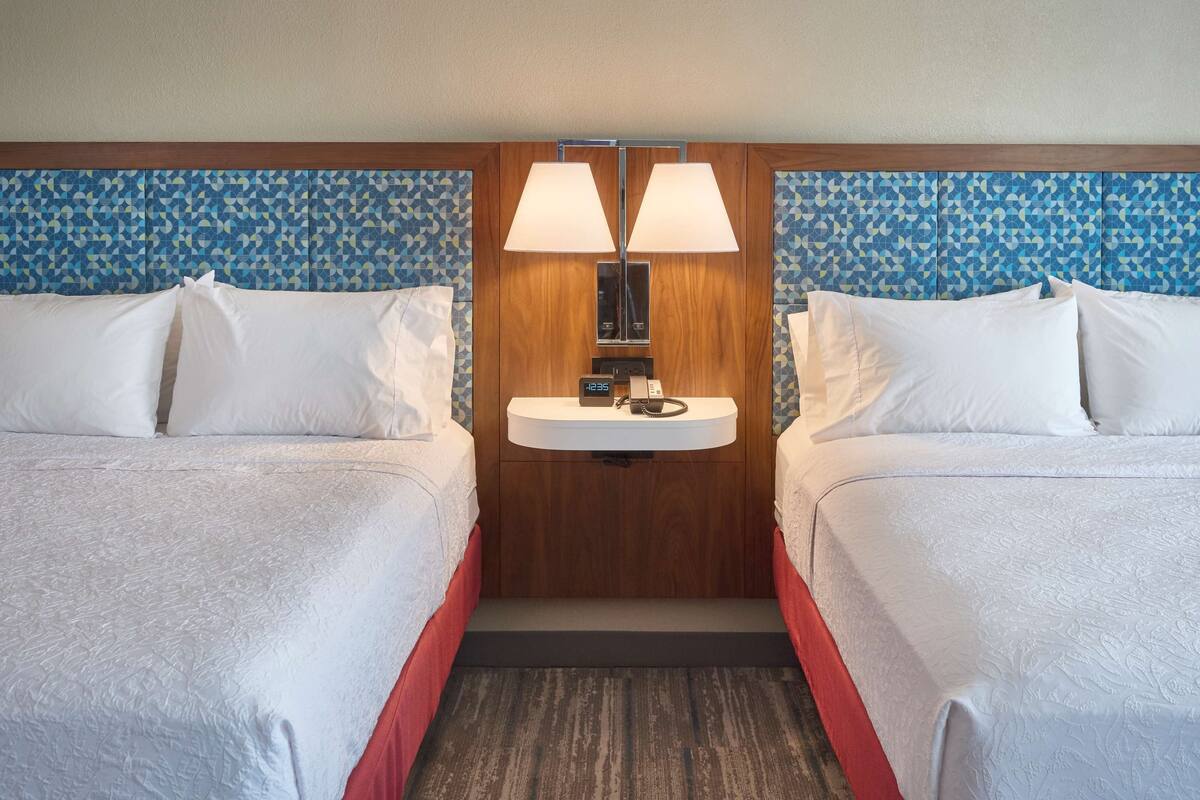 A hotel room with two beds, a built-in sink, and a clock above it.
