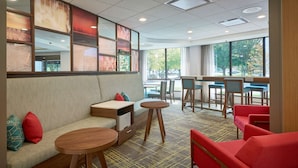 A modern lounge area with a sofa, round tables, and red chairs. - Hampton Inn by Hilton Harrisburg West (Mechanicsburg)