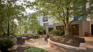 An outdoor patio area with seating, a garden, and a modern building in the background. - Hampton Inn by Hilton Harrisburg West (Mechanicsburg)