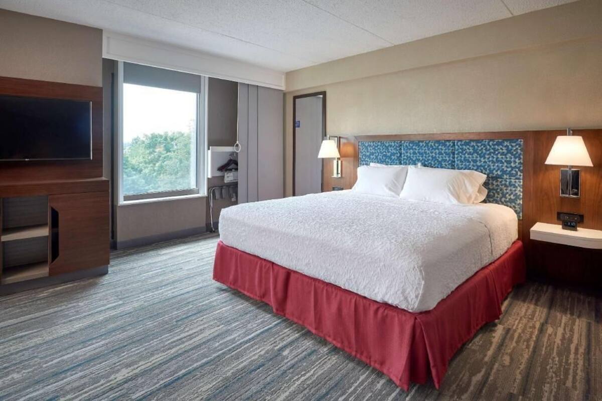 A hotel room with a large bed, a TV, a desk, and a window.