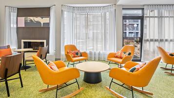 A modern lounge area with orange rocking chairs, a round table, and a fireplace.