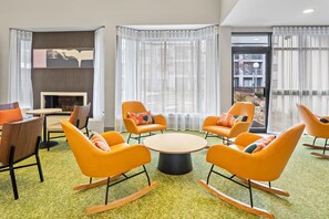 A modern lounge area with orange rocking chairs, a round table, and a fireplace.