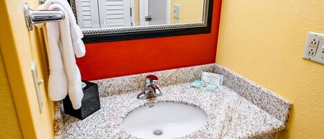 Un baño con lavamanos de encimera de granito, un espejo con marco negro y un perchero con toallas blancas.