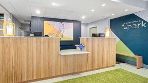 A modern hotel reception area with wooden reception desks, a large abstract wall art piece, and a 'It only takes a spark' sign. - Spark by Hiton Bettendorf Quad Cities (Bettendorf)