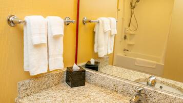 Une salle de bain avec un lavabo doté d’un plan de travail en granit, un miroir et une douche visible au fond.
