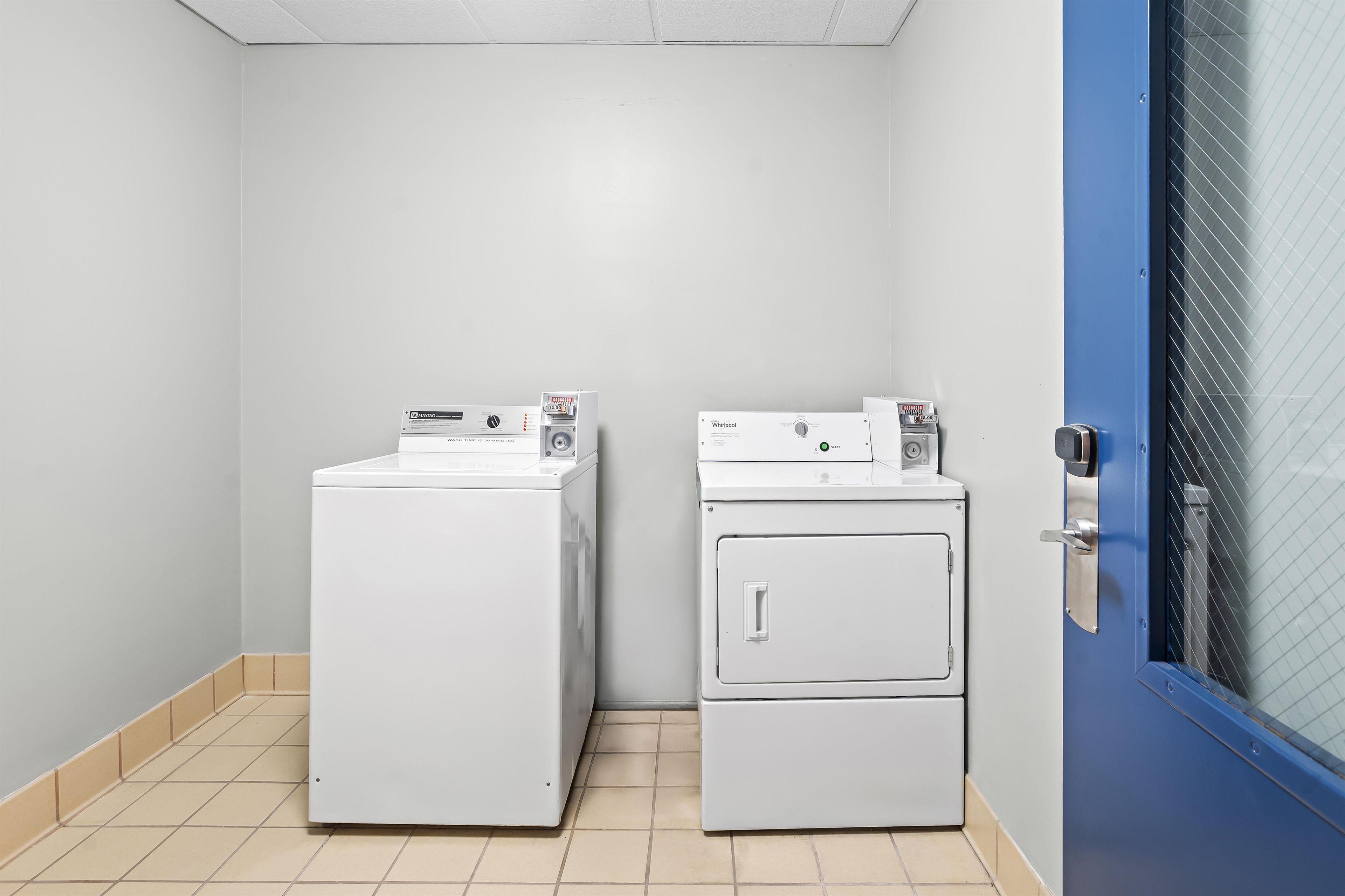 A laundry room with two stacked washers and dryers, a blue door, and a tiled floor.