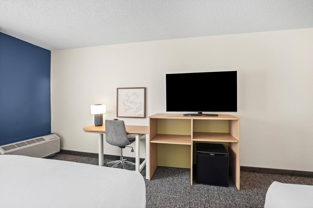 Une chambre d’hôtel comprenant un lit, un bureau avec une chaise, une télévision et une petite poubelle.