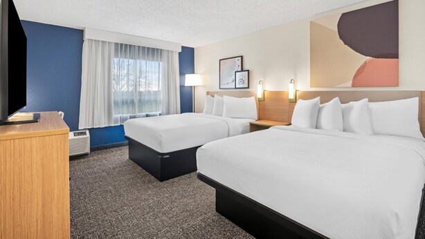 A hotel room with two beds, a desk, a TV, and a large abstract painting on the wall. - Spark by Hiton Bettendorf Quad Cities (Bettendorf)