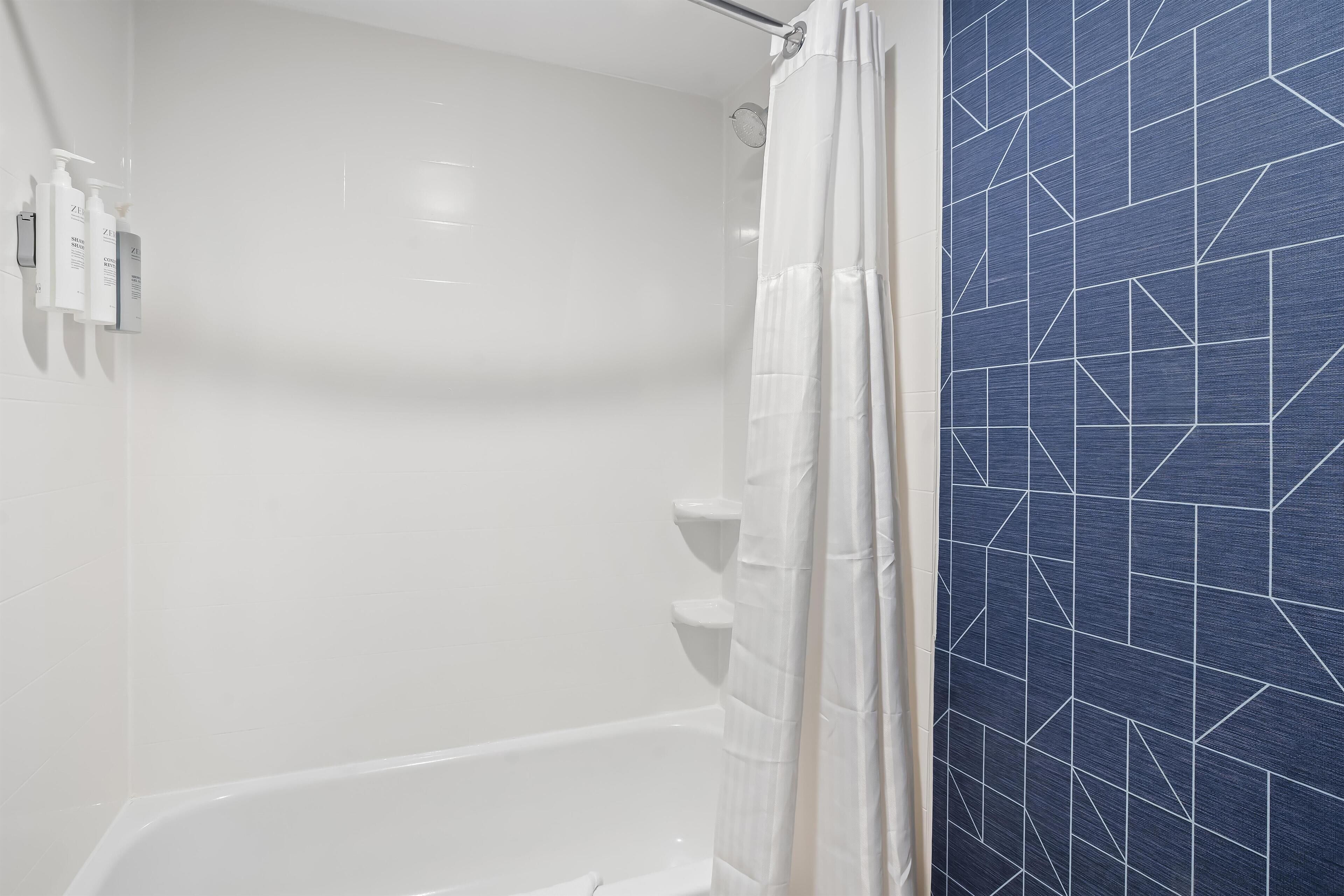 Un baño con una bañera blanca, una cortina de ducha y una pared con un diseño geométrico de azulejos.