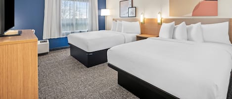 Habitación de hotel con dos camas, televisión, escritorio y ventana con cortinas.