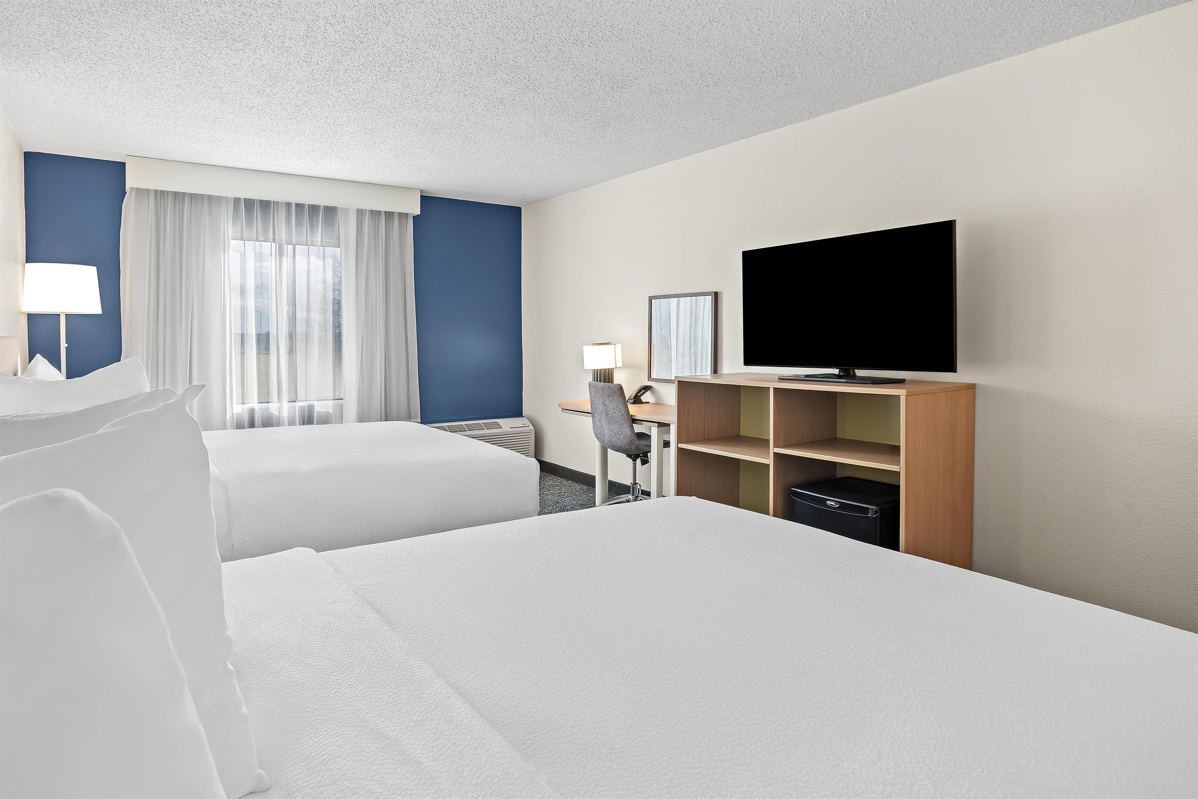 Habitación de hotel con dos camas, un escritorio, una silla, un televisor y una ventana con cortinas.
