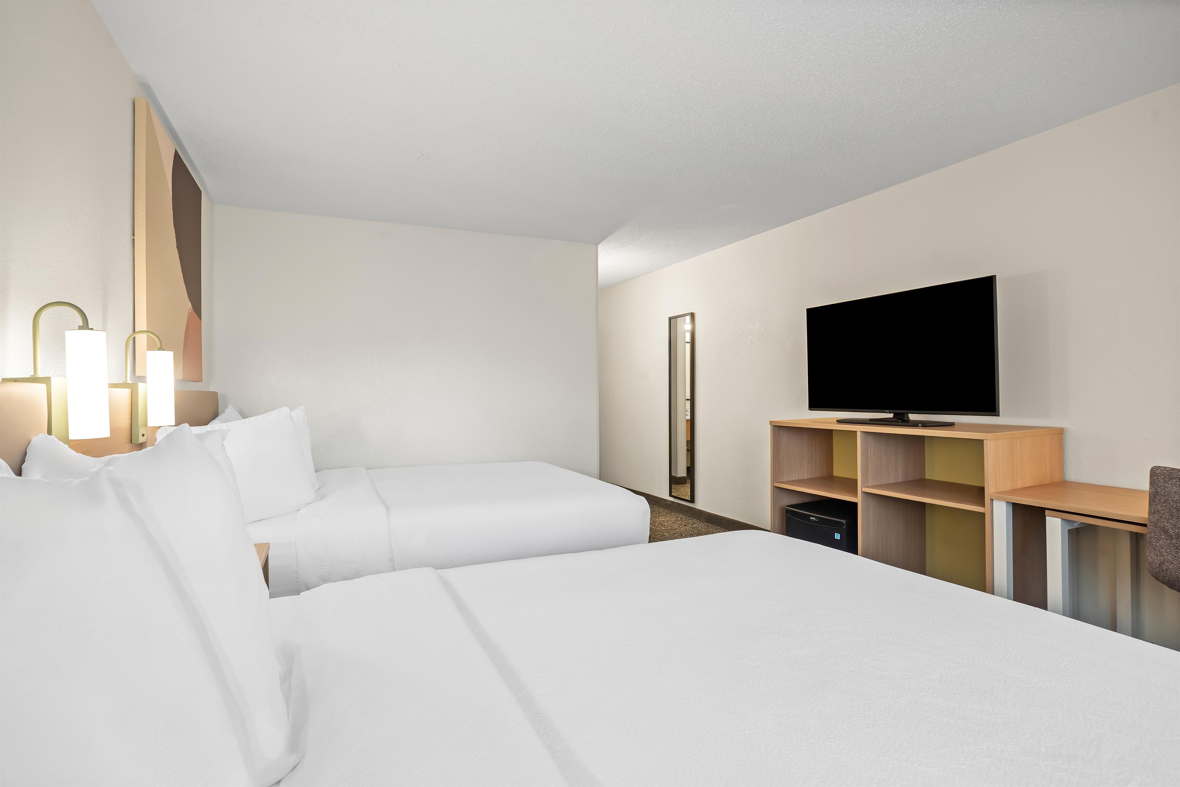 A hotel room with two beds, a TV, a mirror, and a desk with a chair.