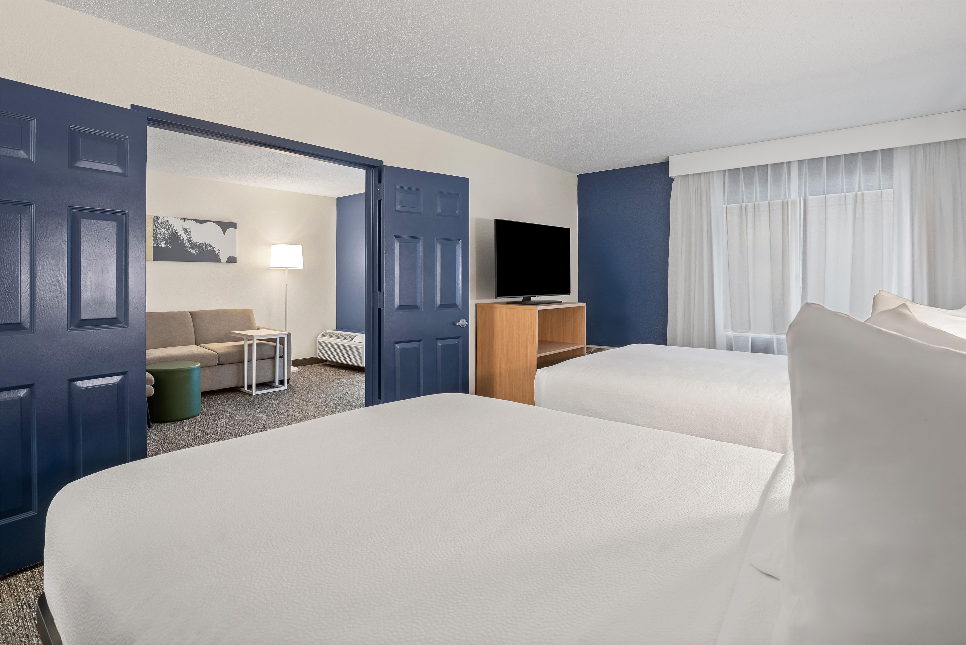 A hotel room with two beds, a TV, a sofa, a lamp, and a window with curtains.