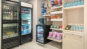 A refrigerated display area with various beverages and snacks, including bottled water, soda, and packaged food items. - Spark by Hiton Bettendorf Quad Cities (Bettendorf)
