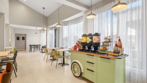 A modern kitchen with a green island, stainless steel appliances, and a dining area with chairs and tables. - Spark by Hiton Bettendorf Quad Cities (Bettendorf)