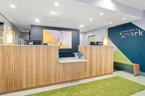 Una reception con finiture in legno, una parete blu con il testo 'It only takes a spark' e un tappeto verde.