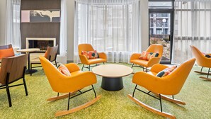 A modern lounge area with orange rocking chairs, a round table, and a fireplace. - Spark by Hiton Bettendorf Quad Cities (Bettendorf)