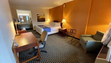 Habitación de hotel con cama, escritorio, silla y una mesita. Hay una lámpara en el escritorio y una silla junto a la cama.