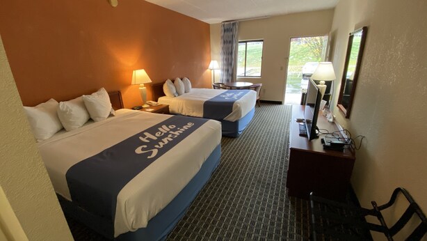 A hotel room with two beds, a desk, a chair, a TV, and a window with a view of greenery. - Days Inn by Wyndham Morehead (Morehead)