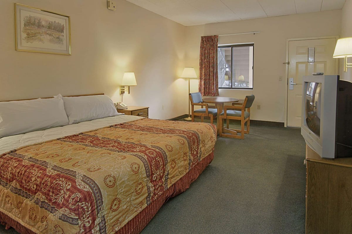 A hotel room with a large bed, a desk with a chair, a television, and a window with curtains.
