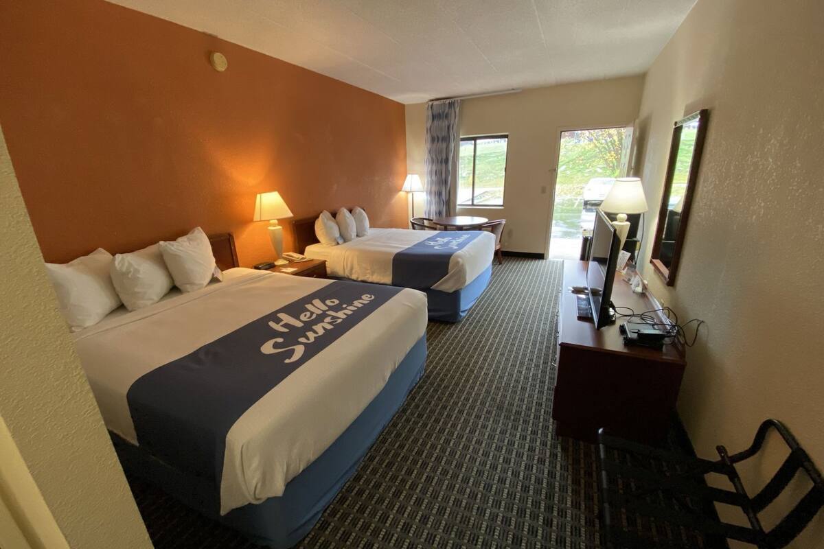 A hotel room with two beds, a desk, a chair, and a window with a view.
