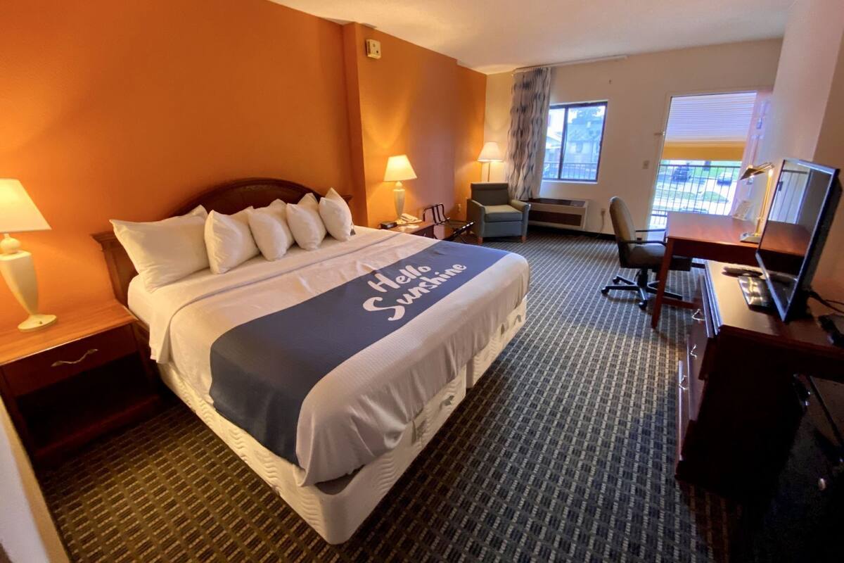 A hotel room with a bed, desk, chair, lamp, and a window.